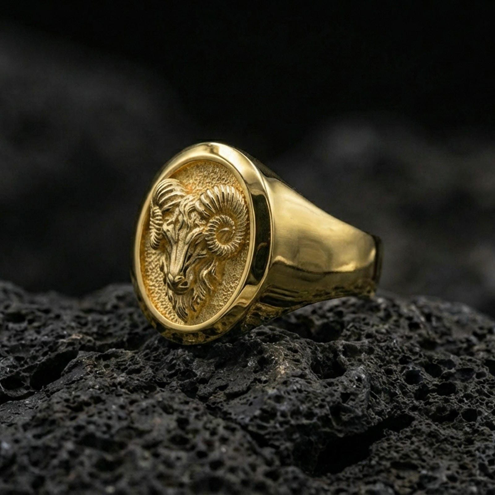 Gold plated ram signet ring on black volcanic rock, close-up emphasizing the horn texture and bold oval frame