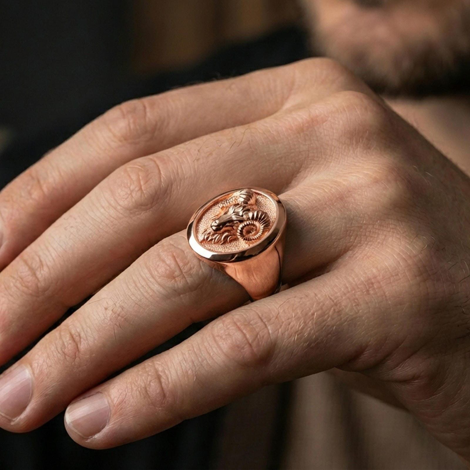 Rose gold plated ram signet ring worn on a finger, macro detail on the horns and sculpted animal face