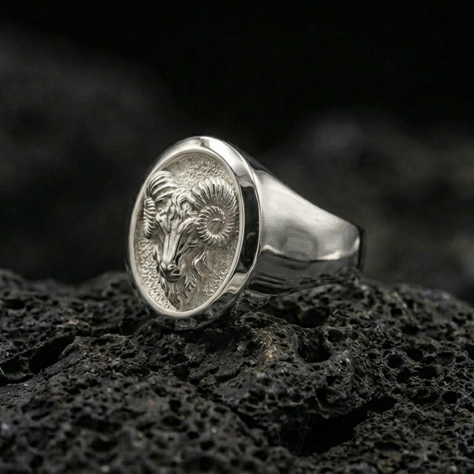 Polished silver ram head ring on textured volcanic stone, macro focus on the curved horns and face detail