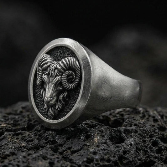 Close-up of an oxidized sterling silver ram signet ring on porous volcanic rock with dark premium lighting