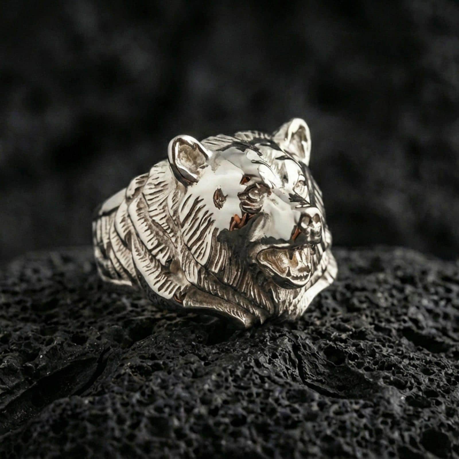 Polished silver bear ring on textured volcanic stone, macro focus on the carved fur and defined facial contours