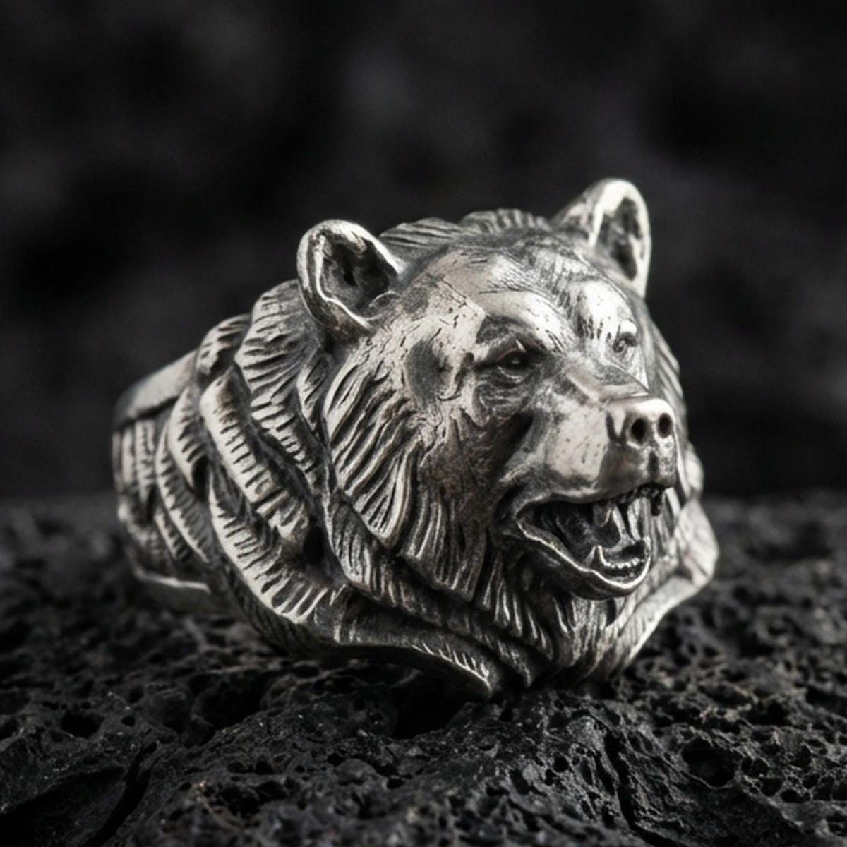 Close-up of an oxidized sterling silver bear head ring on porous volcanic rock with dark premium studio lighting