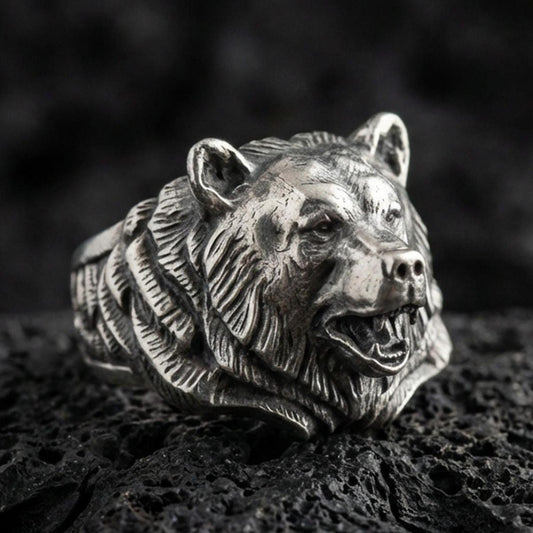 Close-up of an oxidized sterling silver bear head ring on porous volcanic rock with dark premium studio lighting