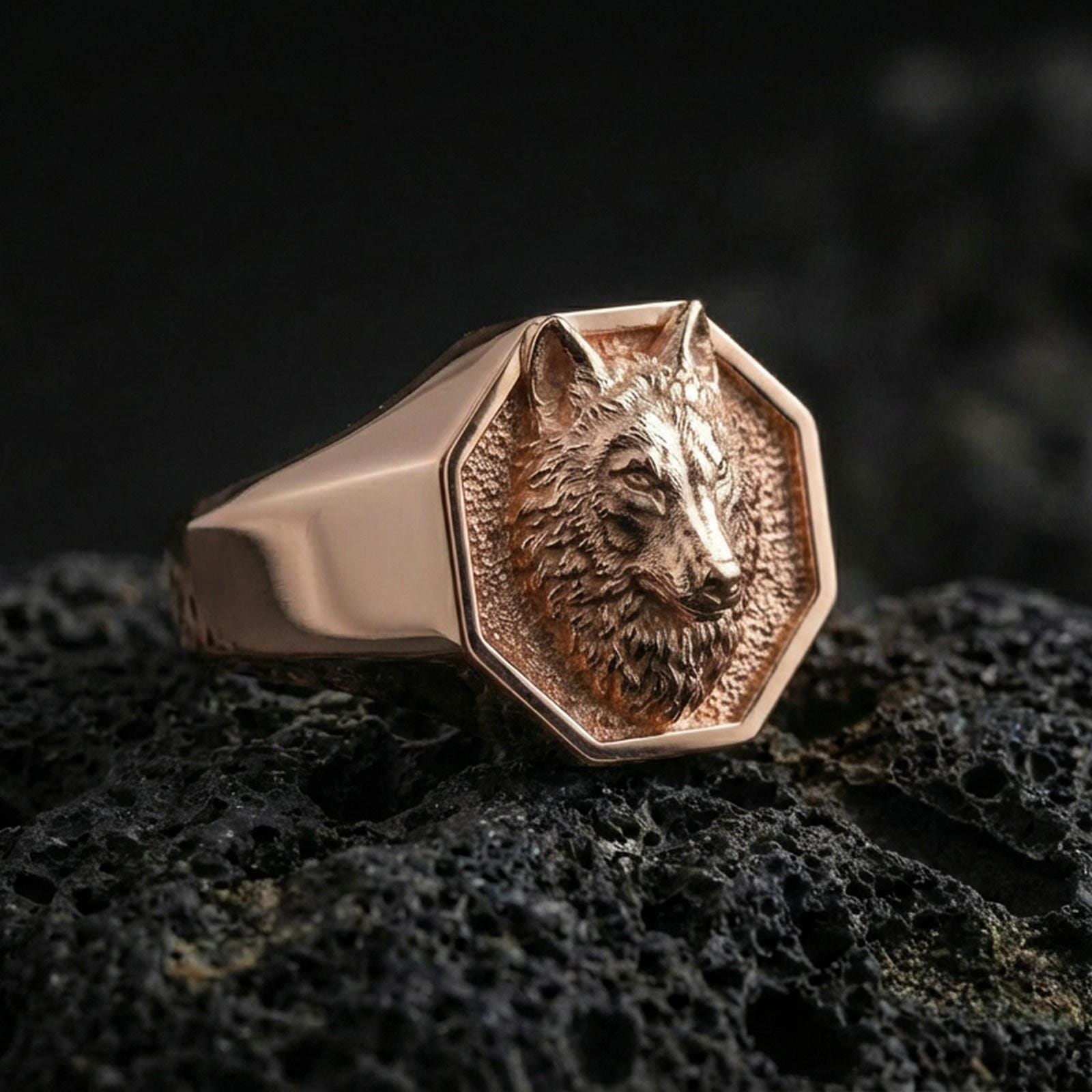 Rose gold plated wolf head signet ring on porous volcanic rock with controlled highlights and deep shadows