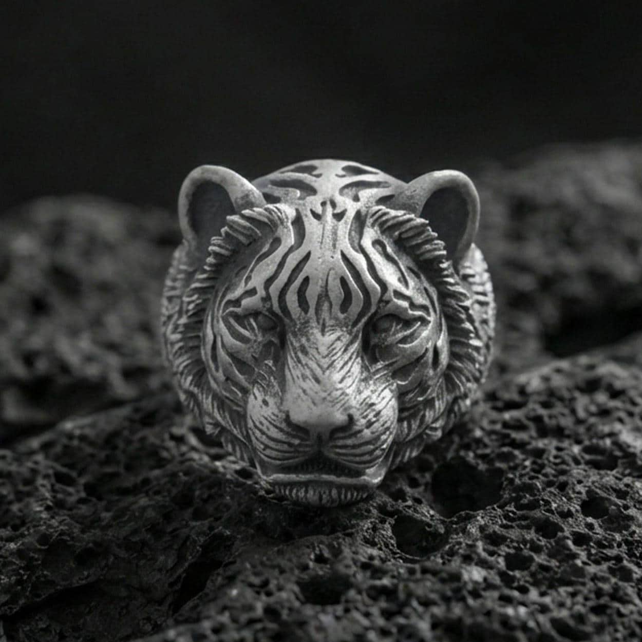 Close-up of an oxidized sterling silver tiger head ring on porous volcanic rock with dramatic studio shadows