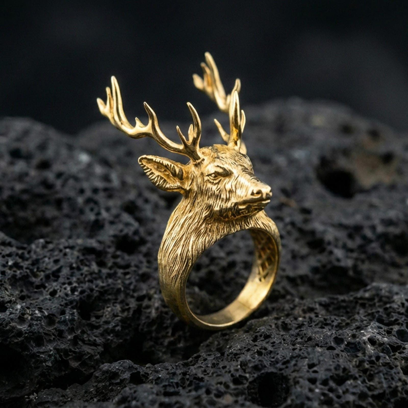 Gold plated stag head ring on black volcanic rock, close-up emphasizing the antler silhouette and texture