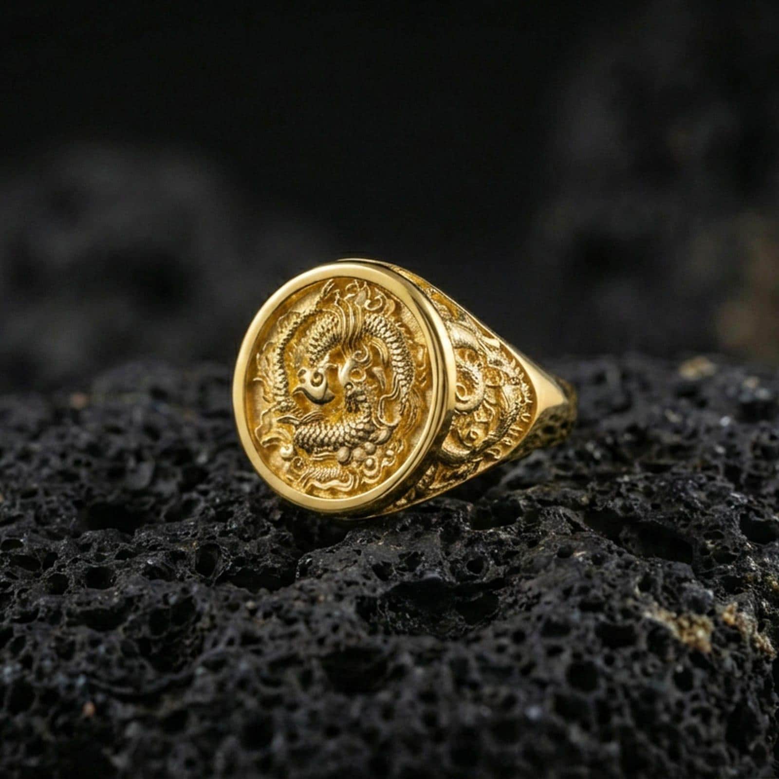Gold plated yin yang koi signet ring on black volcanic rock, close-up highlighting the relief details