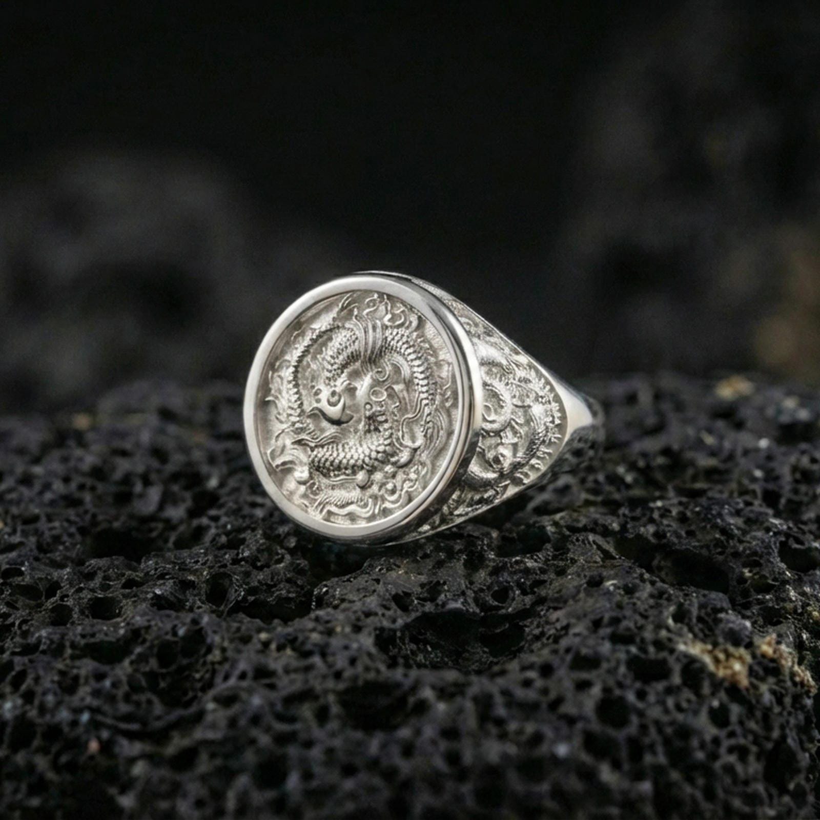 Polished silver koi fish ring on textured volcanic stone, macro focus on the engraved yin yang koi design