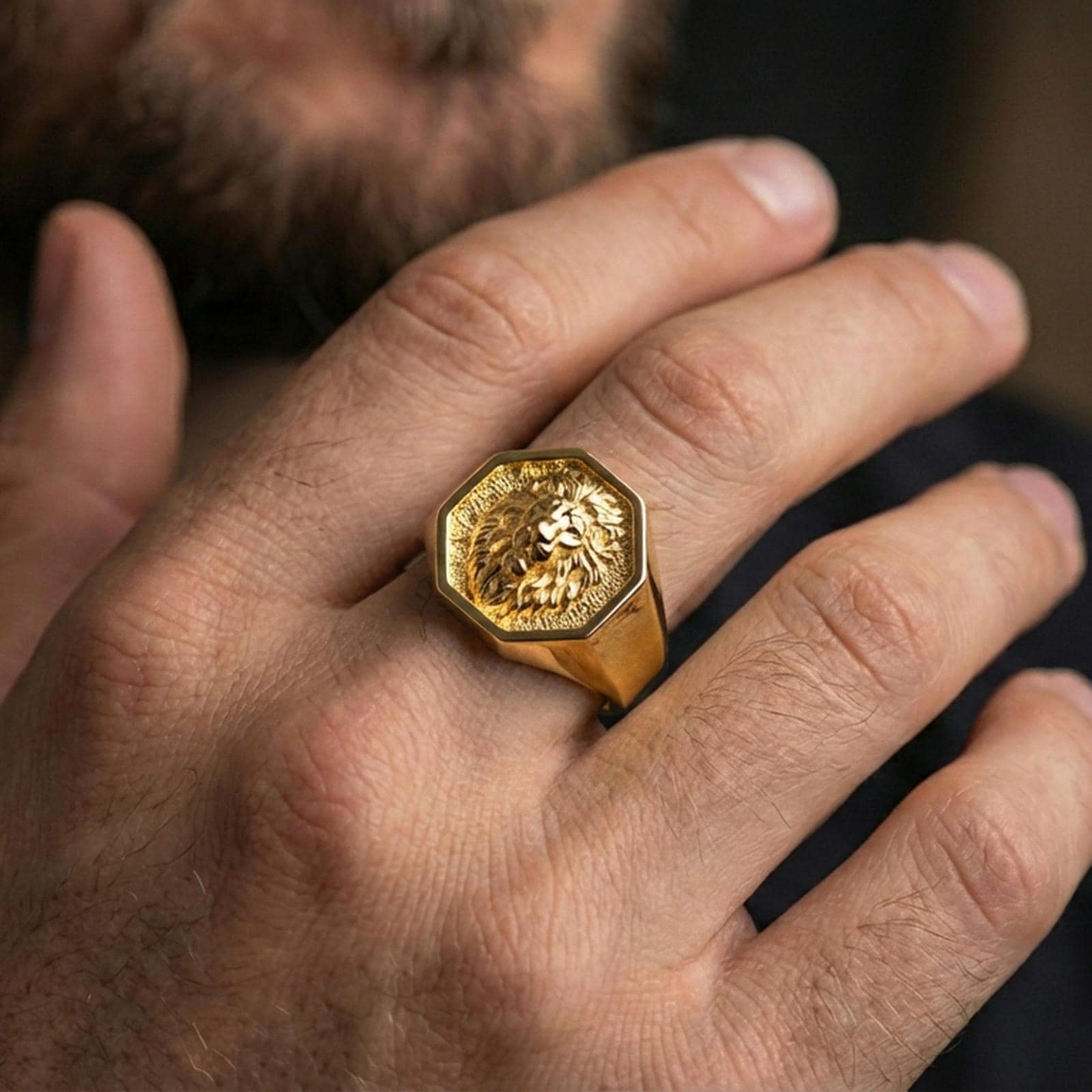 Gold plated lion signet ring worn on a finger, luxury styling against a dark background
