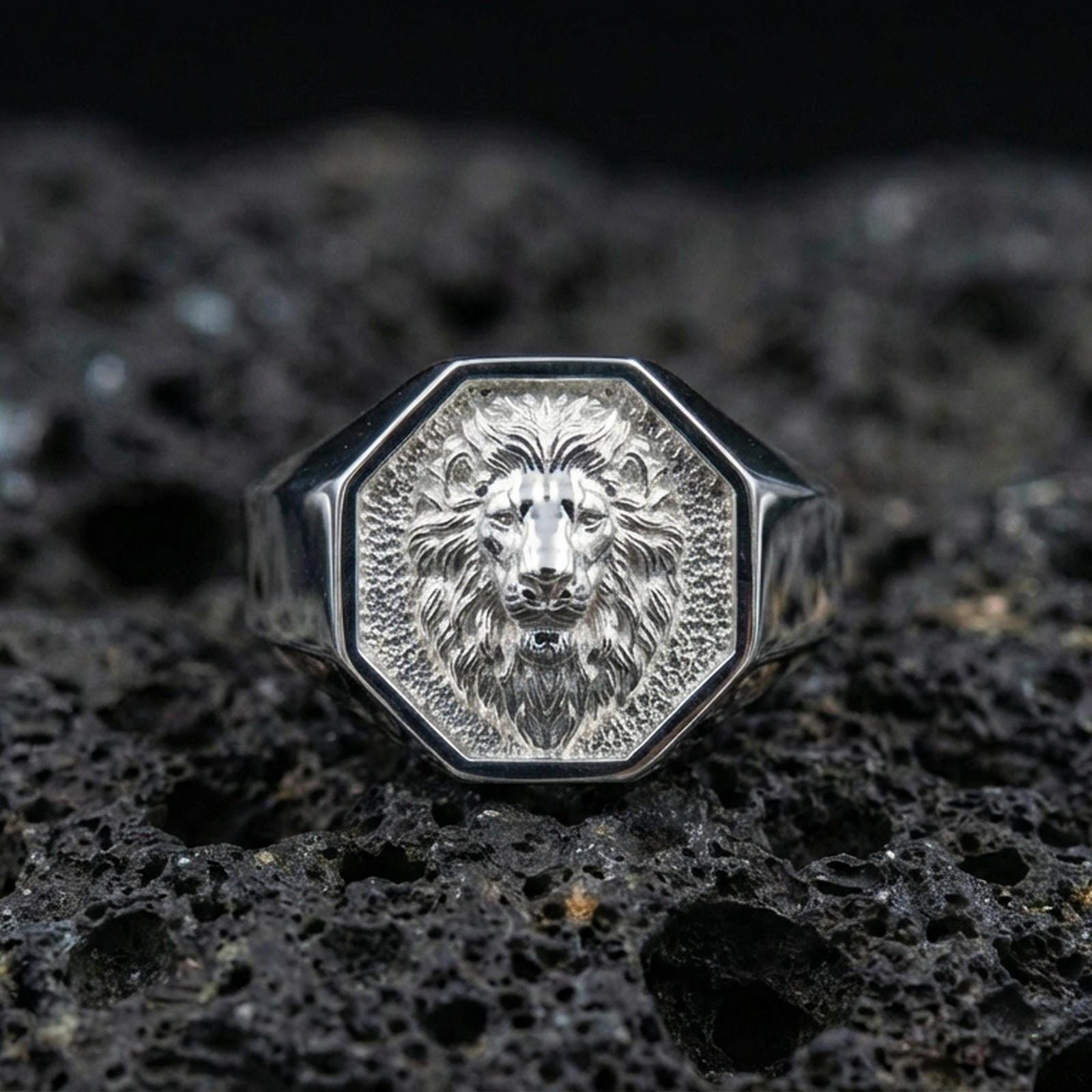 Polished silver geometric lion ring on textured volcanic stone, macro focus on the lion face engraving