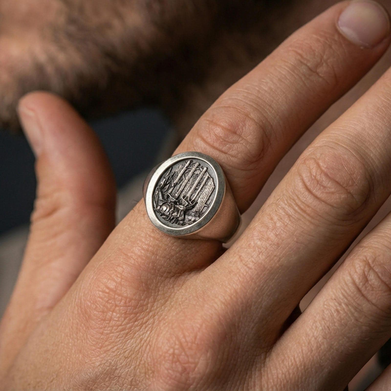 Oxidized sterling silver forest signet ring worn on a finger, close-up showing the engraved trees and wildlife detail