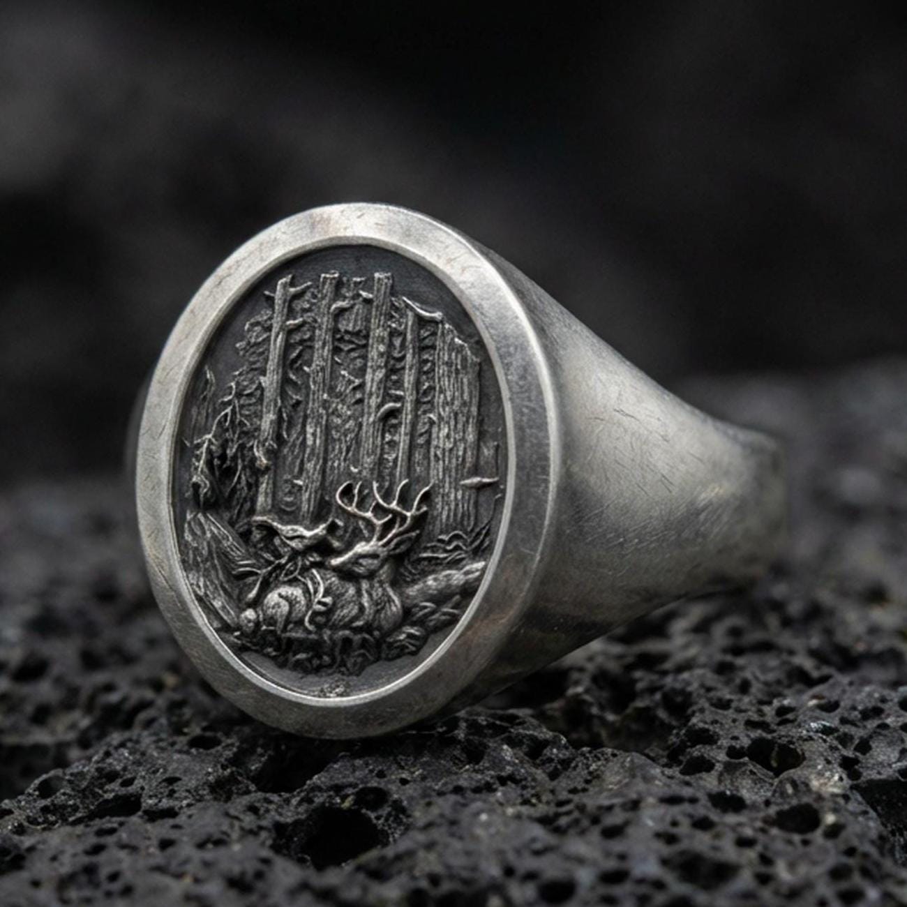 Close-up of an oxidized sterling silver forest engraved signet ring on porous volcanic rock in a dark studio