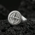 Load image into Gallery viewer, Sterling silver compass ring in a polished silver finish, round signet face with detailed compass rose and directional markings, close-up on volcanic stone
