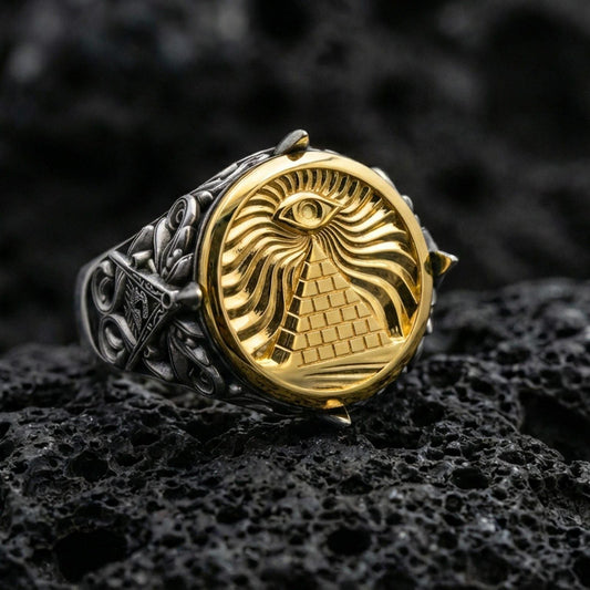 Sterling silver all-seeing eye pyramid signet ring with an oxidized body and gold plated front, engraved radiant eye and brick pyramid motif, macro on black volcanic rock