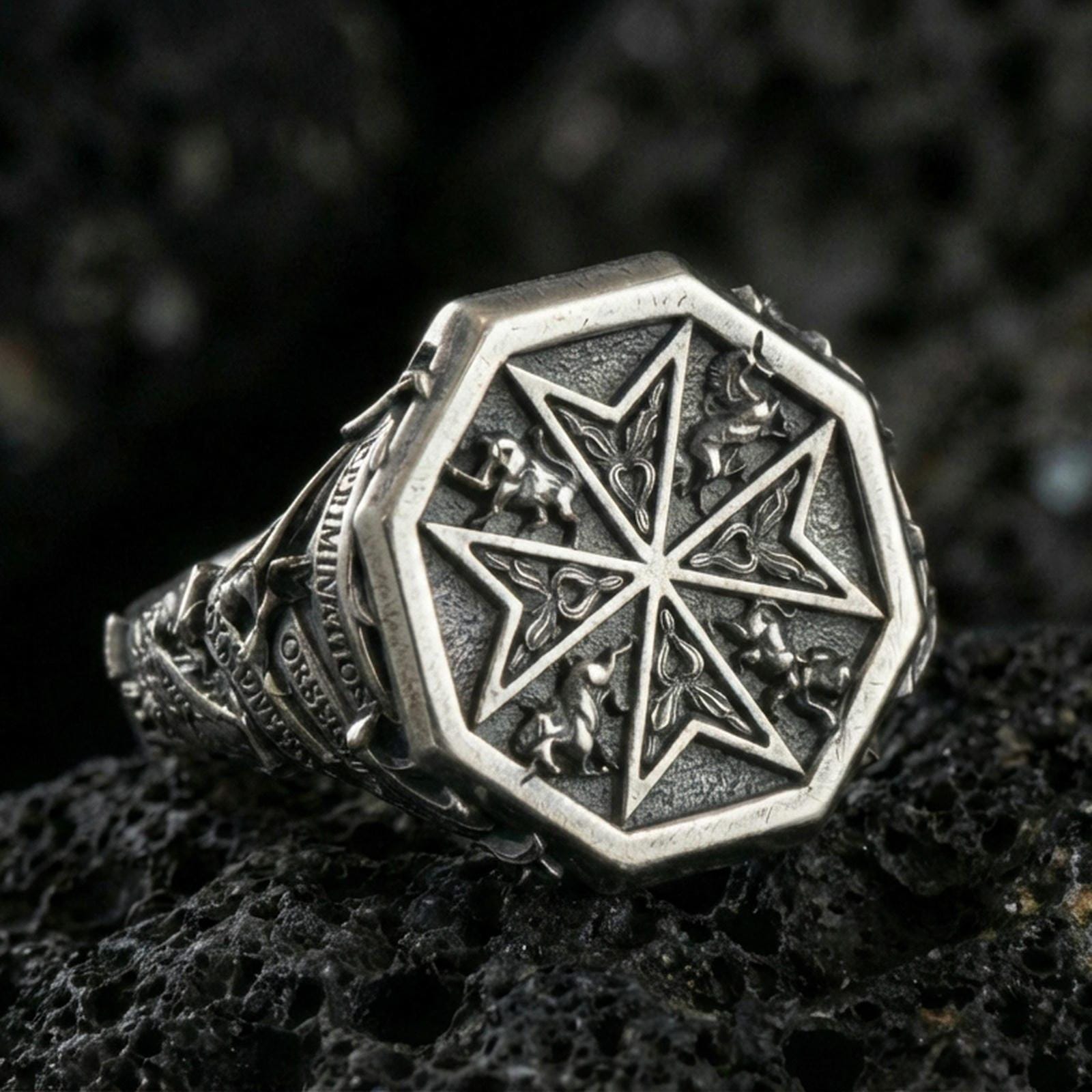 Sterling silver Maltese cross signet ring with an oxidized finish, octagonal face featuring a Crusader-style cross and ornamental relief details, macro on black volcanic rock