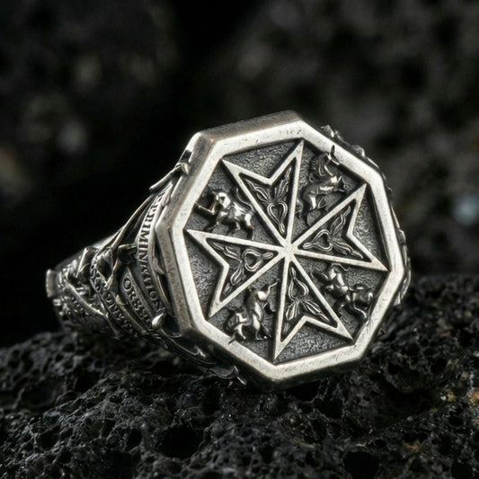 Sterling silver Maltese cross signet ring with an oxidized finish, octagonal face featuring a Crusader-style cross and ornamental relief details, macro on black volcanic rock