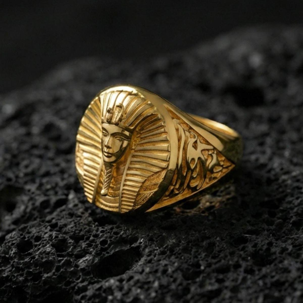 Sterling silver Egyptian king ring with a gold plated finish, oval signet design showing a pharaoh bust with headdress detail and ornate side engravings, macro product shot on volcanic rock