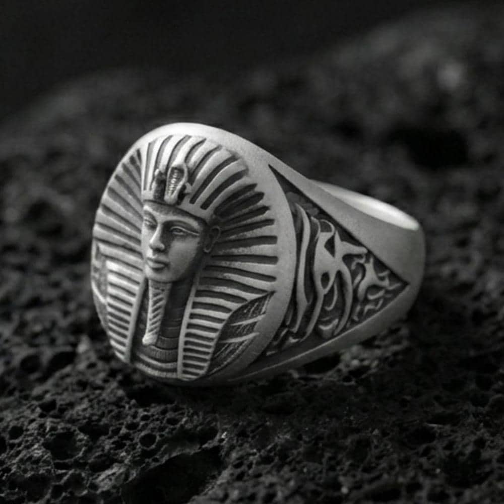 Sterling silver Egyptian pharaoh signet ring with an oxidized finish, oval face featuring a detailed royal pharaoh portrait and engraved side motifs, macro on black volcanic rock