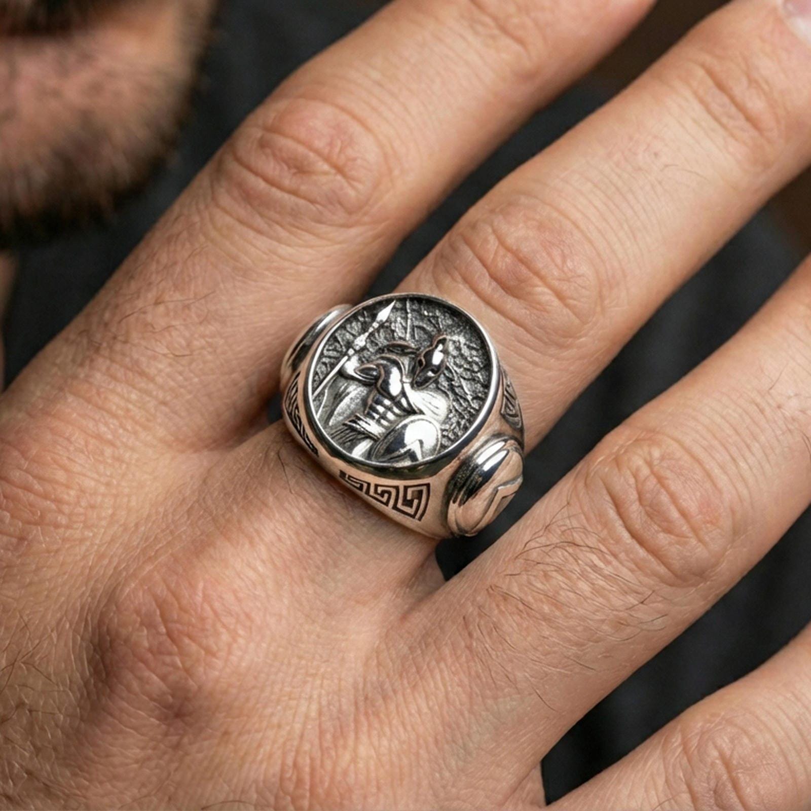 Sterling silver ancient Greek statement ring on a finger, macro lifestyle image emphasizing the polished silver hoplite relief with spear and shield details