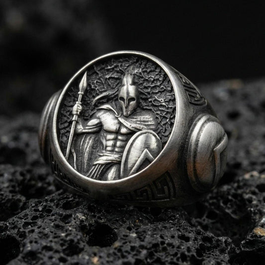 Sterling silver Greek warrior signet ring with an oxidized finish, round face featuring a helmeted Spartan-style soldier holding a spear and shield, macro on black volcanic rock