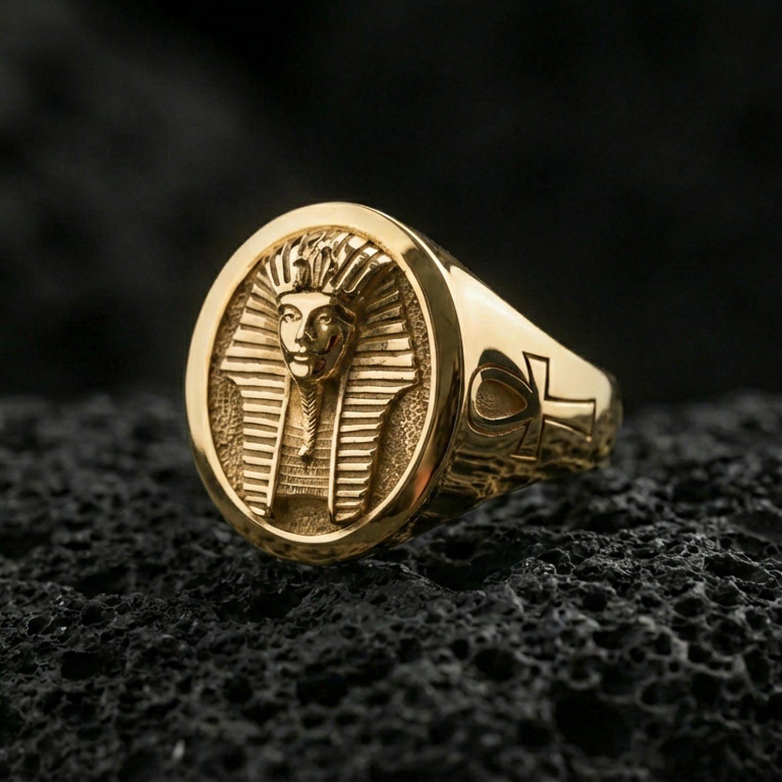 Sterling silver ancient Egypt signet ring with a gold plated finish, oval face showing a pharaoh portrait with geometric headdress lines and side ankh motif, macro product shot on volcanic rock