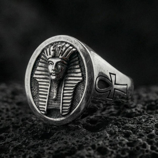 Sterling silver Egyptian pharaoh signet ring with an oxidized finish, oval face featuring a carved ancient king bust and side ankh symbol, macro on black volcanic rock
