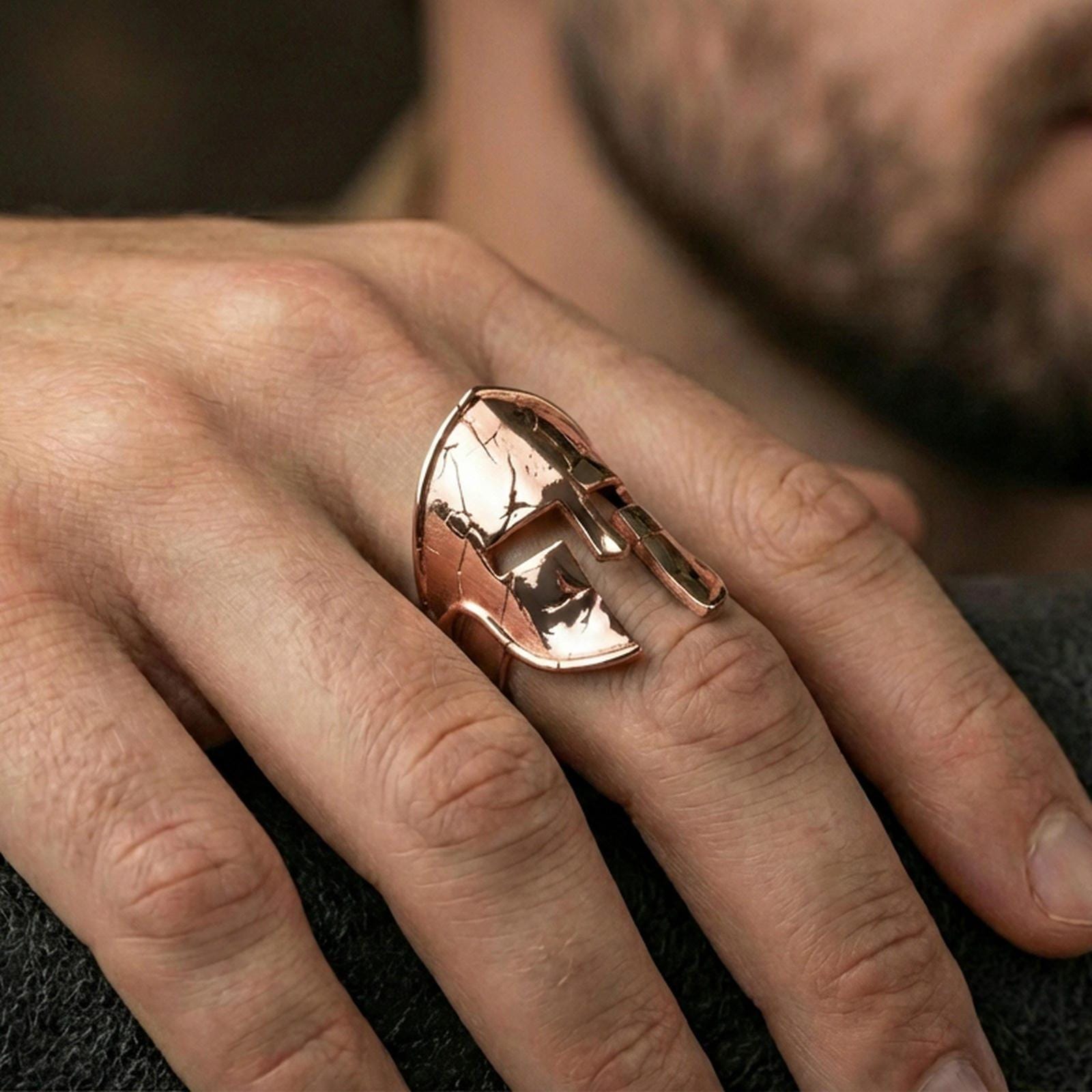 Sterling silver Spartan helm ring on a finger, macro lifestyle shot featuring the rose gold plated finish and battle-worn cracked helmet detailing
