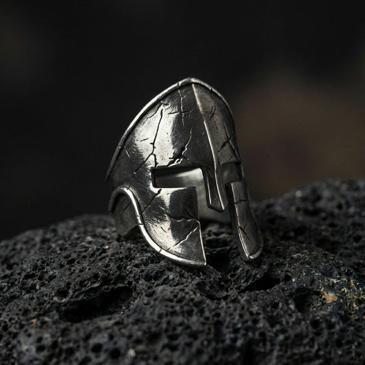 Sterling silver Spartan warrior helmet signet ring with an oxidized finish, ancient Greek helmet design with cracked texture detail, macro on black volcanic rock