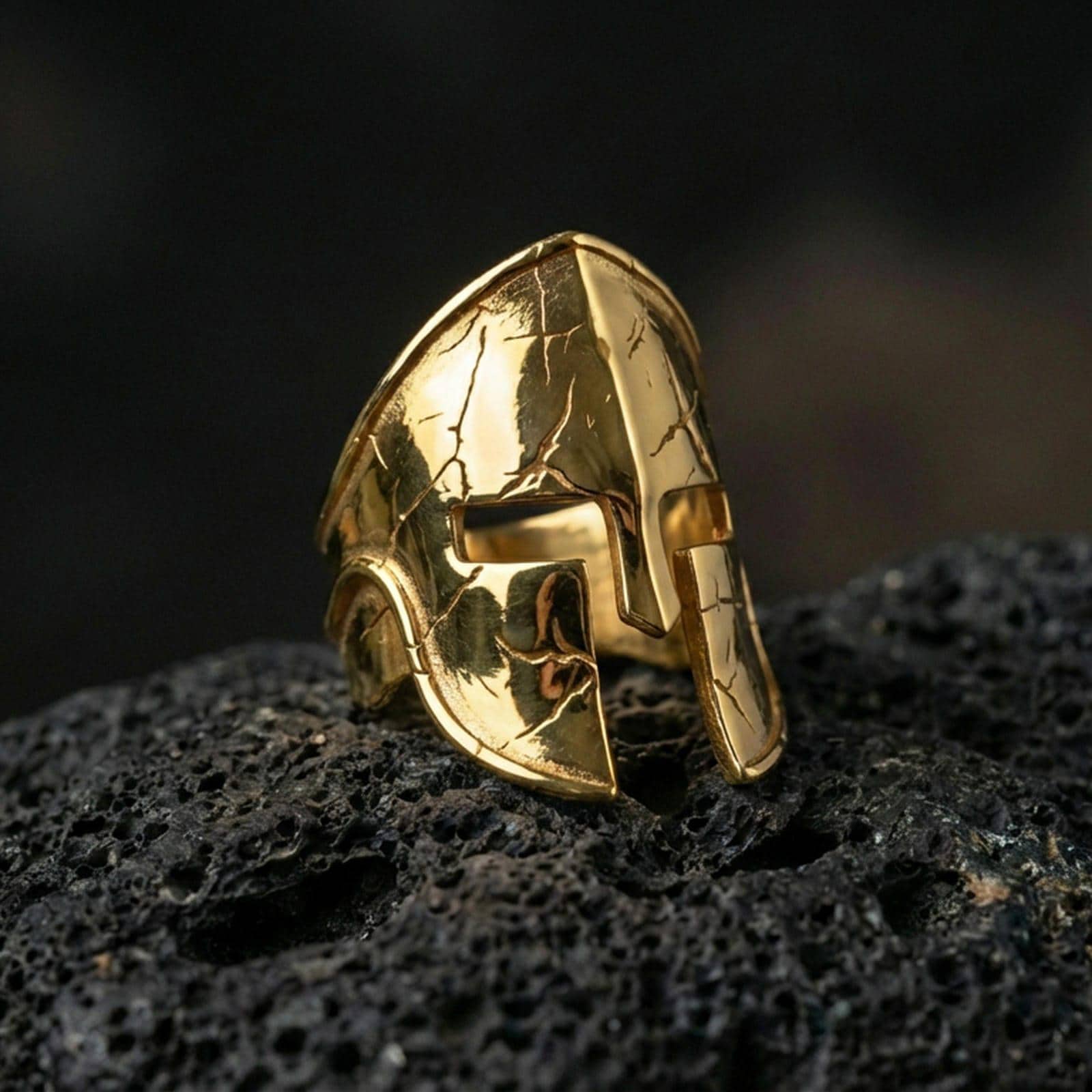 Sterling silver ancient Greek Spartan helmet ring with a gold plated finish, detailed warrior helm signet design with battle-worn texture, macro product shot on volcanic rock
