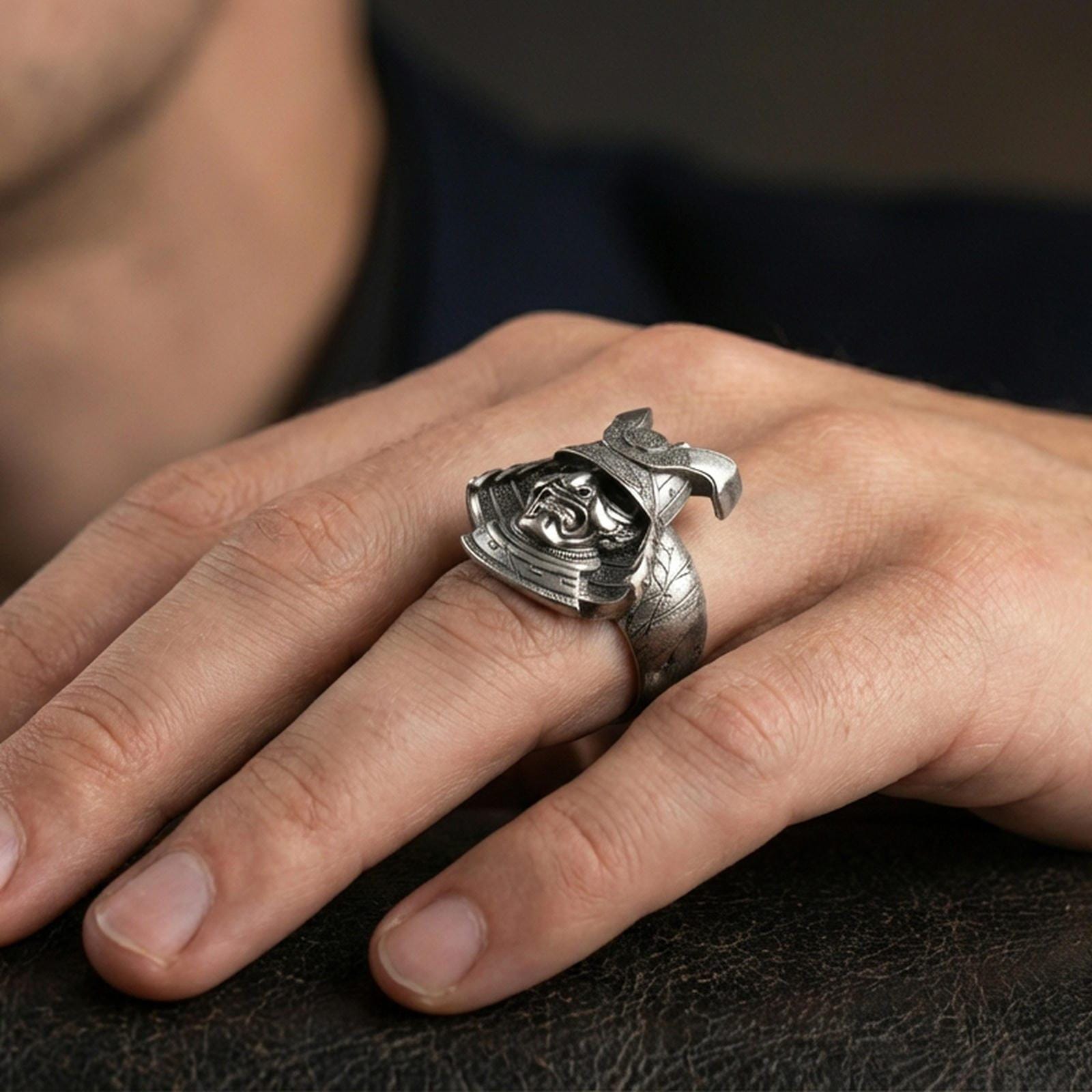 Sterling silver samurai mask ring worn on a finger, close-up lifestyle shot highlighting the oxidized finish and detailed kabuto helmet with fierce warrior face