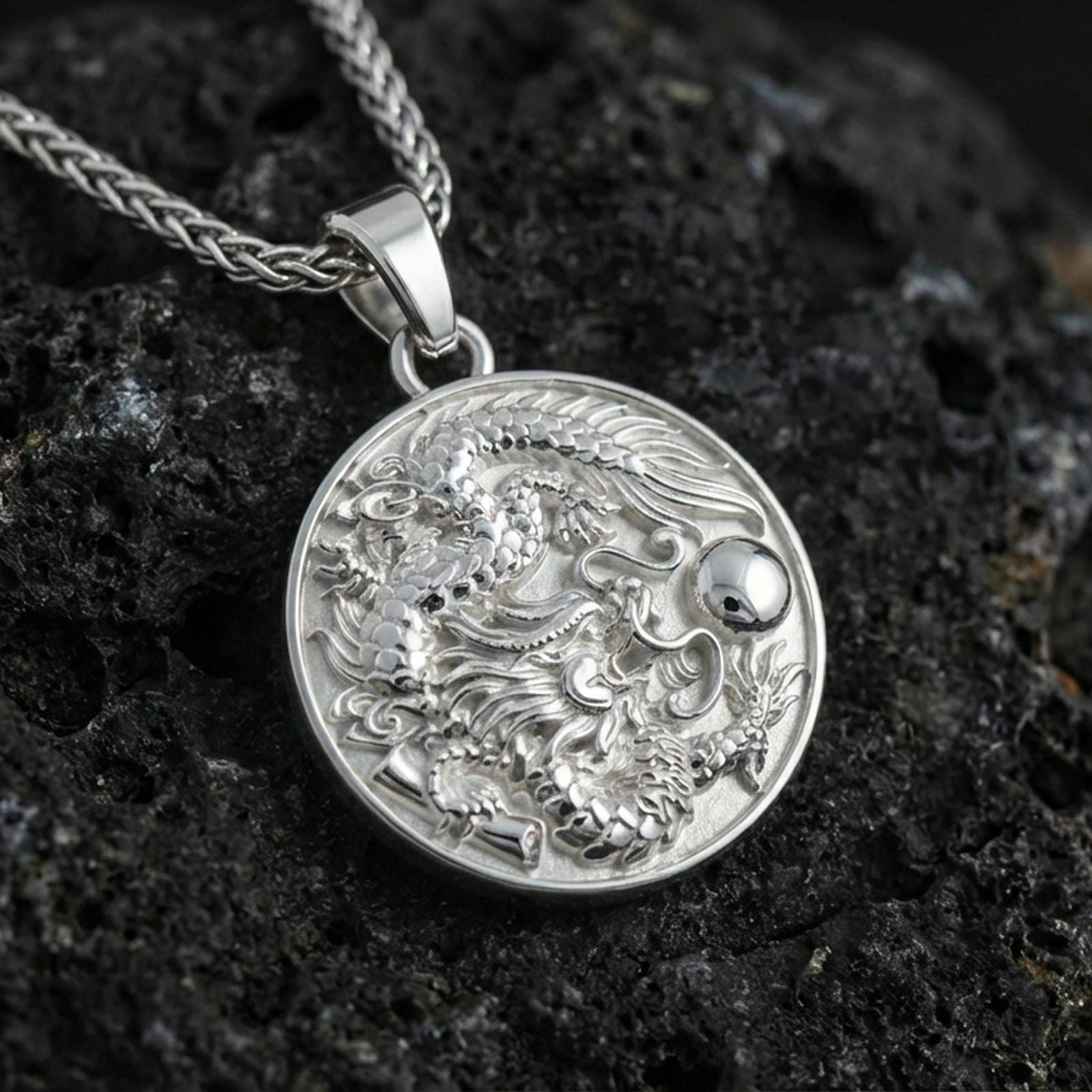 Sterling silver circular dragon pendant in a polished silver finish, high-relief Asian dragon design with textured scales, macro product shot on volcanic stone