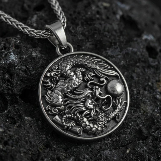 Sterling silver dragon medallion pendant with an oxidized finish, detailed coiled dragon relief with flowing clouds, close-up on black volcanic rock