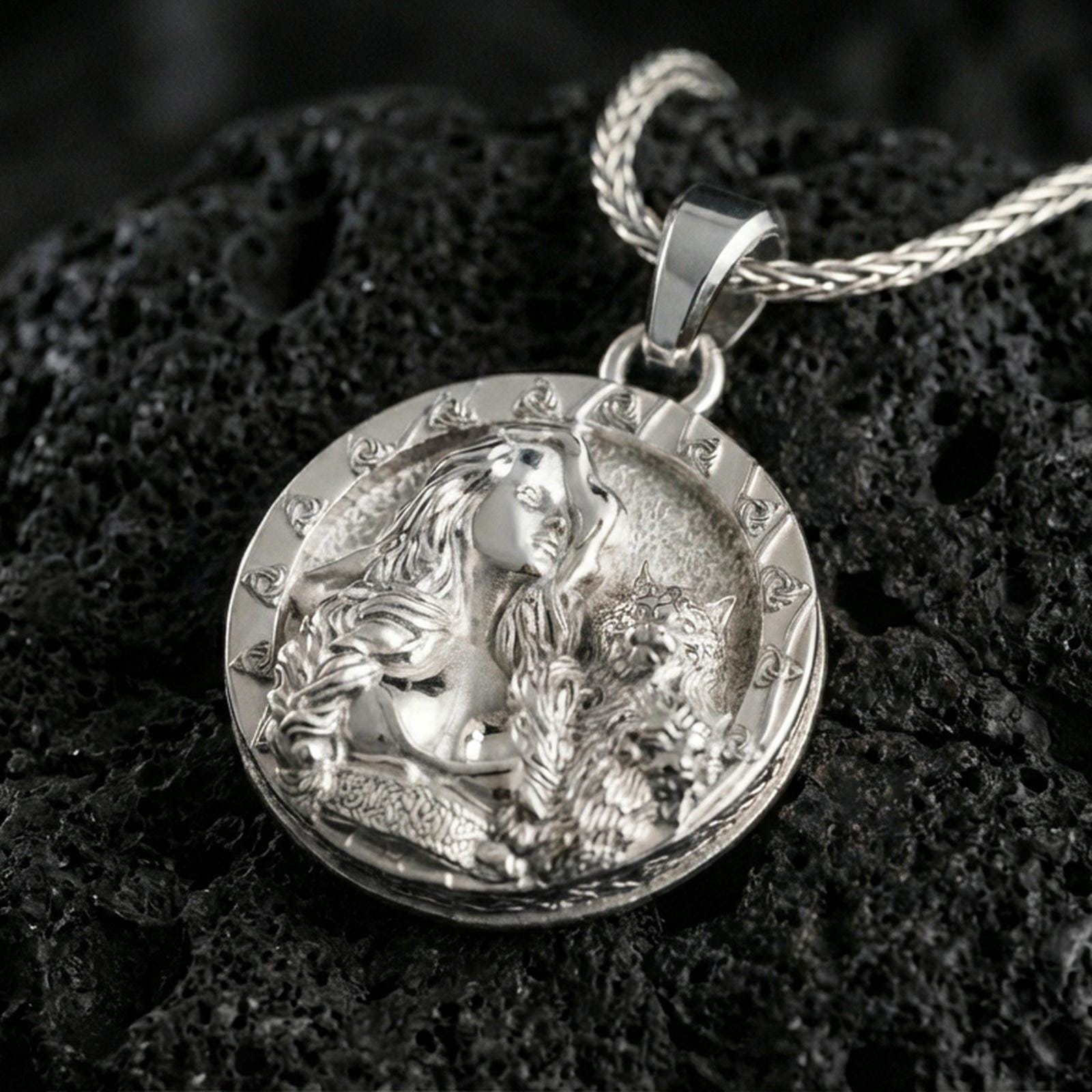 Sterling silver Freya pendant in a polished silver finish, round Norse goddess coin medallion with detailed hair and feline motif, macro on volcanic stone