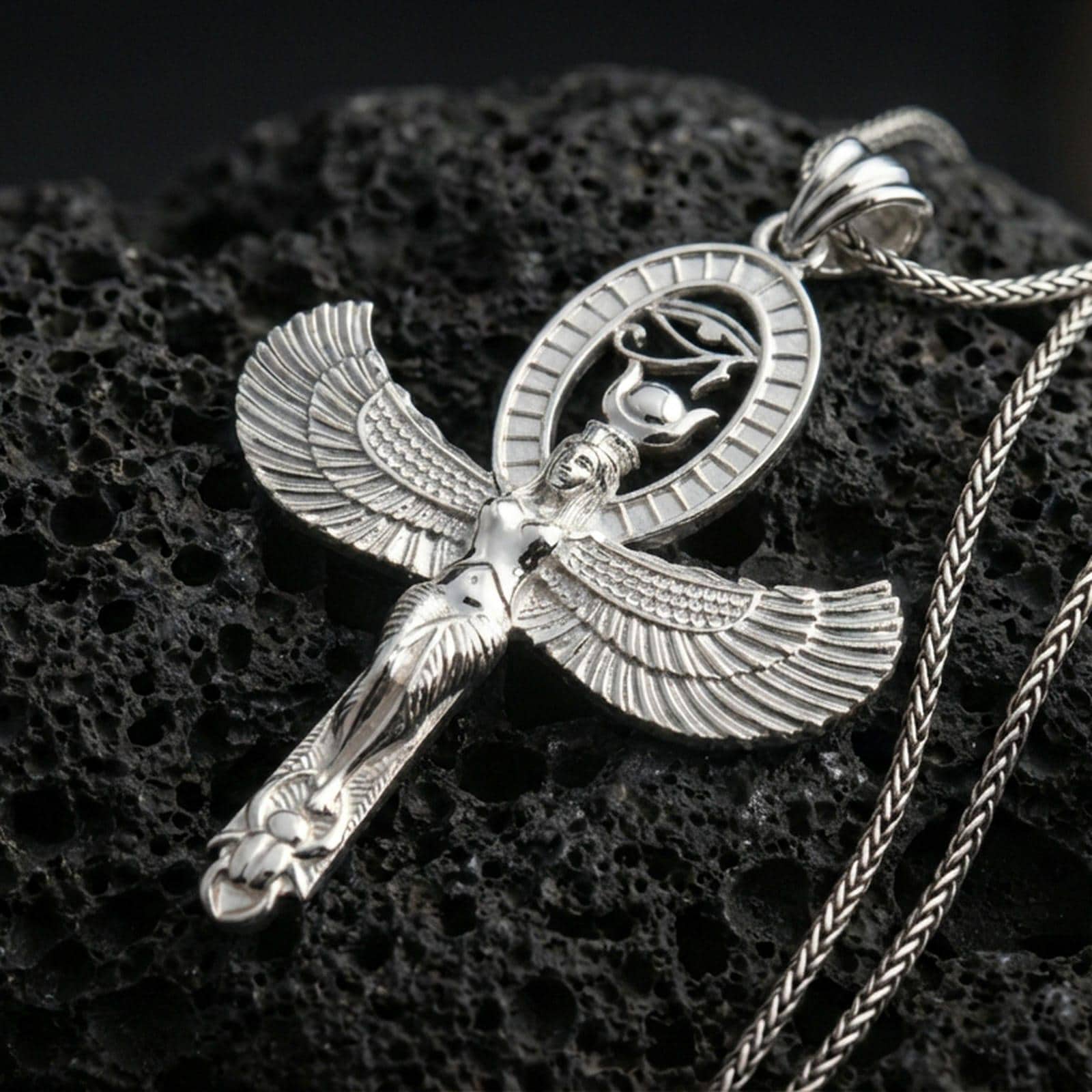 Sterling silver winged Isis pendant in a polished silver finish, Egyptian goddess amulet with detailed feather wings and oval cartouche motif, macro on volcanic stone