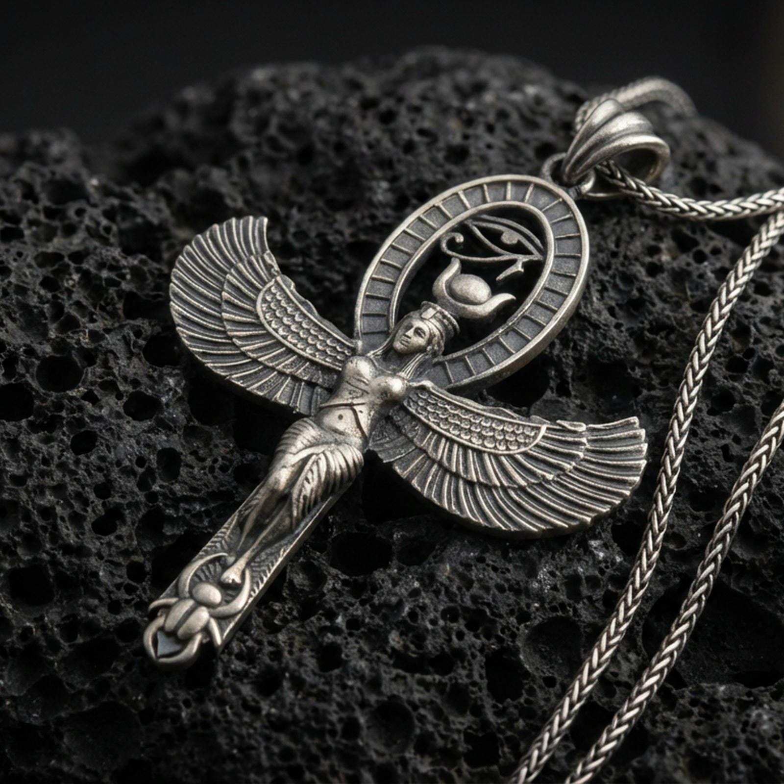 Sterling silver Egyptian Isis winged pendant with an oxidized finish, goddess figure with spread wings and oval hieroglyph halo, close-up on black volcanic rock