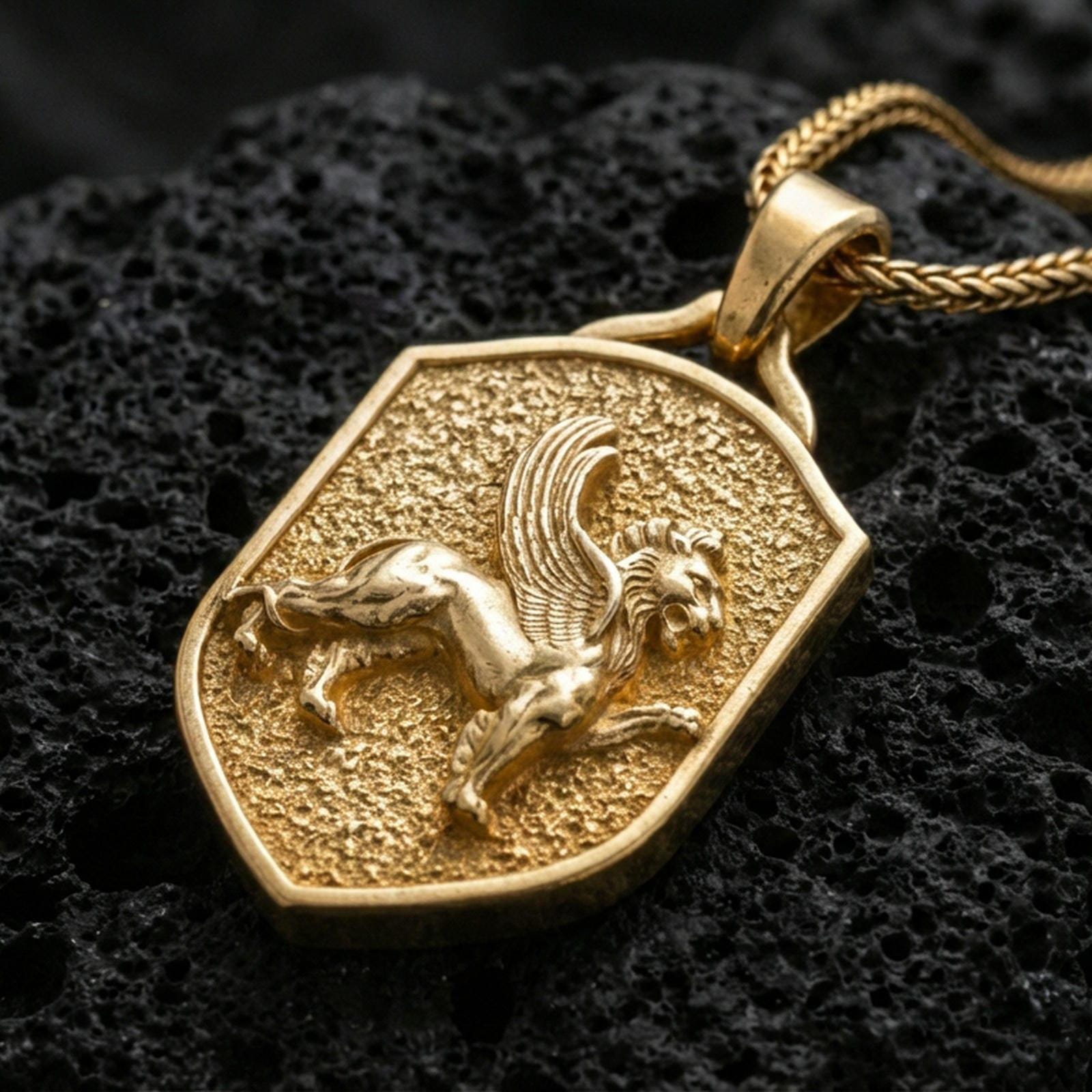 Sterling silver winged lion shield pendant with a gold plated finish, heraldic flying lion emblem on a textured shield, close-up on volcanic rock