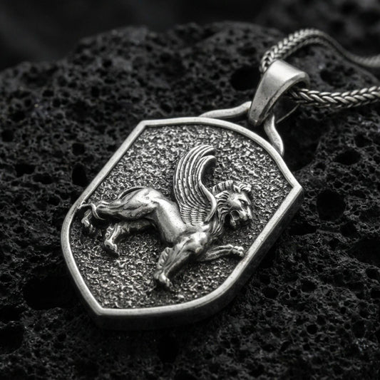 Sterling silver winged lion shield pendant with an oxidized finish, medieval heraldic griffin-style motif in raised relief, close-up on black volcanic rock