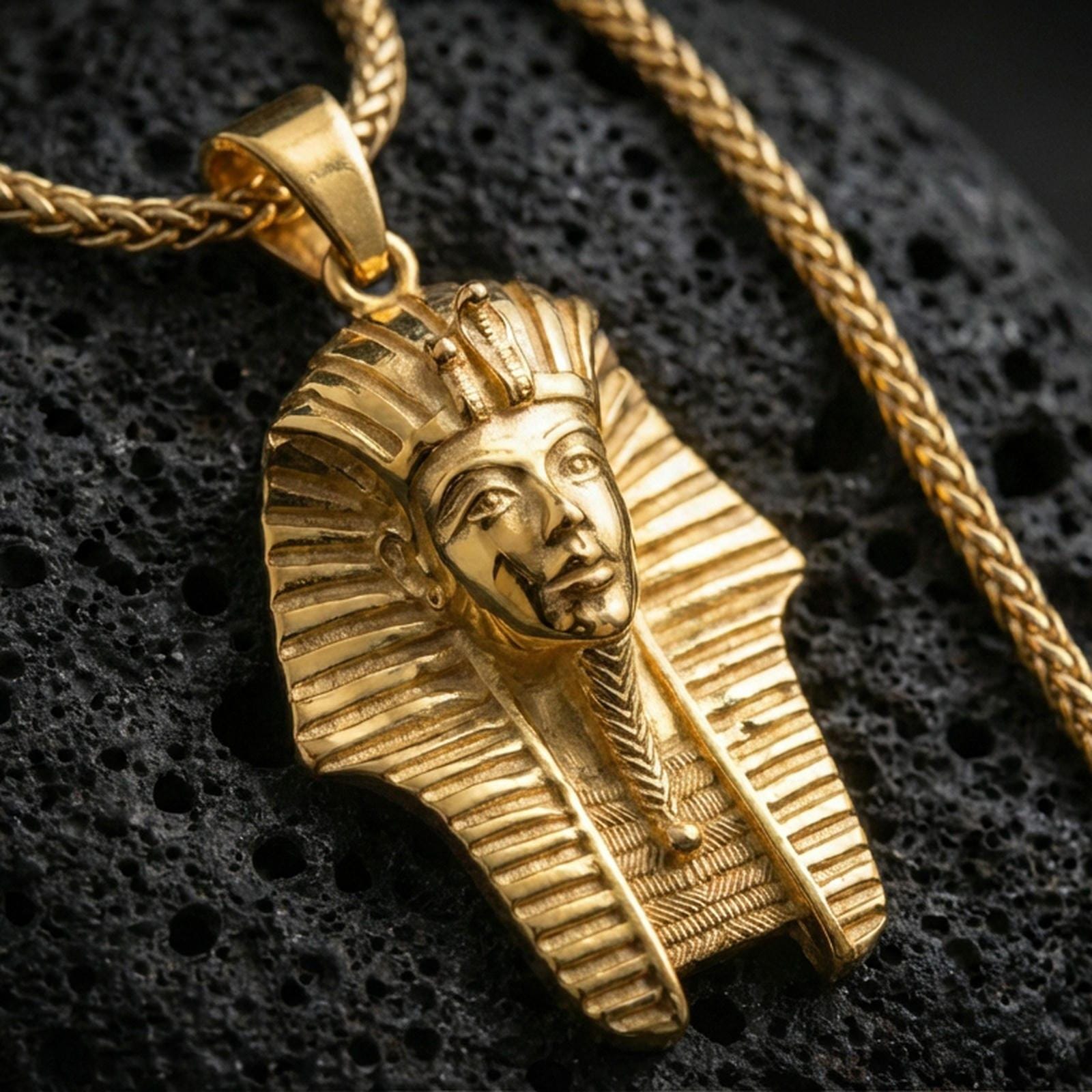 Sterling silver pharaoh head pendant with a gold plated finish, Egyptian king headdress design in high relief, close-up on volcanic rock