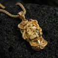 Load image into Gallery viewer, Gold plated Medusa head pendant necklace on textured volcanic rock, premium macro-style photo emphasizing the glossy finish and high-relief snake crown texture.
