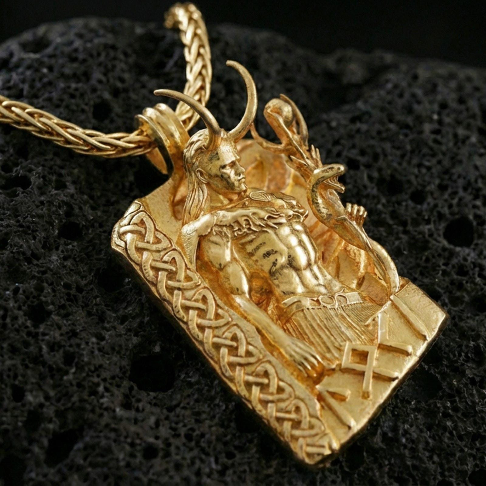 Gold plated Loki pendant necklace on textured volcanic rock, premium close-up showcasing warm reflective shine across the Norse god relief and raised border details.