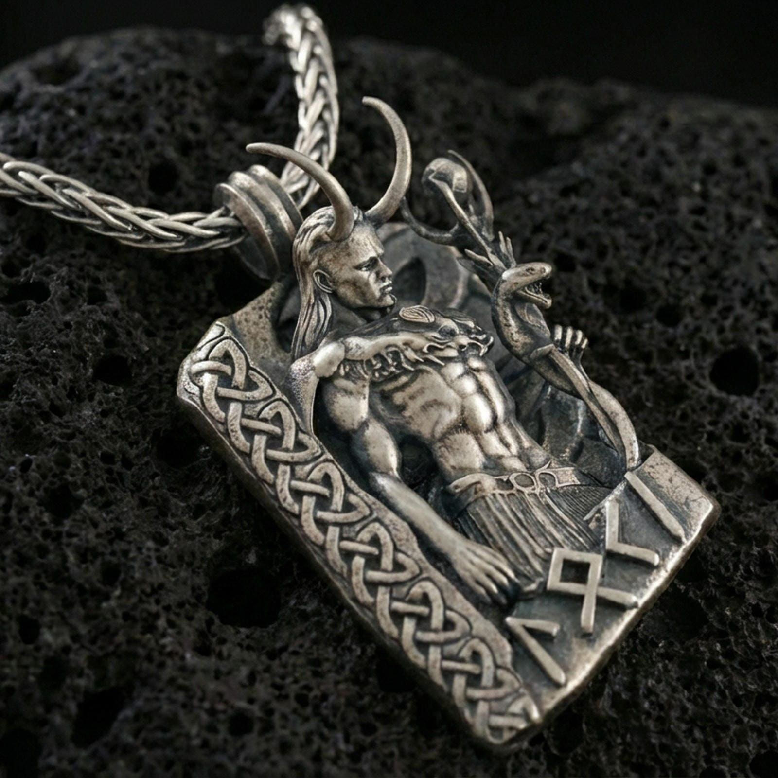Oxidized Loki pendant necklace on textured volcanic rock, close-up centered shot highlighting the horned figure, staff, and deep antique shadowing.