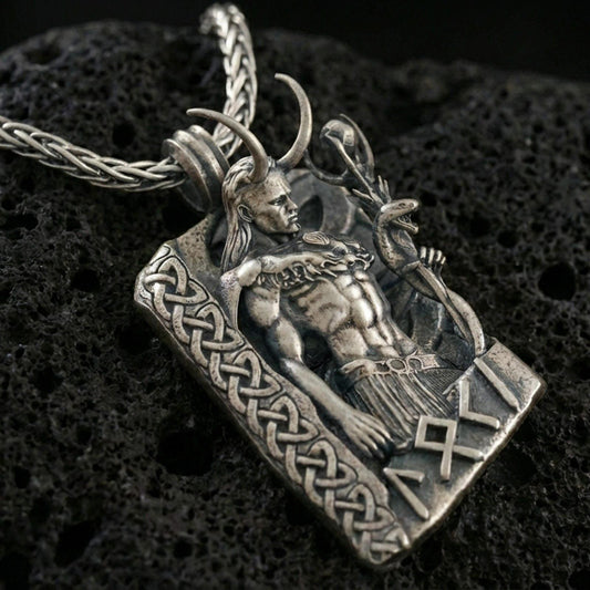 Oxidized Loki pendant necklace on textured volcanic rock, close-up centered shot highlighting the horned figure, staff, and deep antique shadowing.