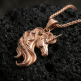 Load image into Gallery viewer, Rose gold plated unicorn head pendant necklace on textured volcanic rock, centered studio-style close-up showcasing a soft rosy glow on the unicorn profile and elegant mane lines.
