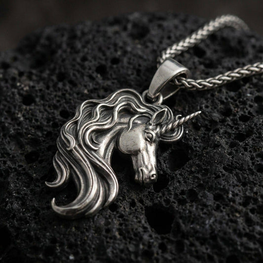 Oxidized unicorn head pendant necklace on textured volcanic rock, centered close-up highlighting the spiraled horn, flowing mane, and antique shadowed depth.
