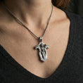 Load image into Gallery viewer, Polished silver gothic cross pendant necklace worn on the neck, clean lifestyle wear shot capturing bright shine and the intricate angel relief in motion.
