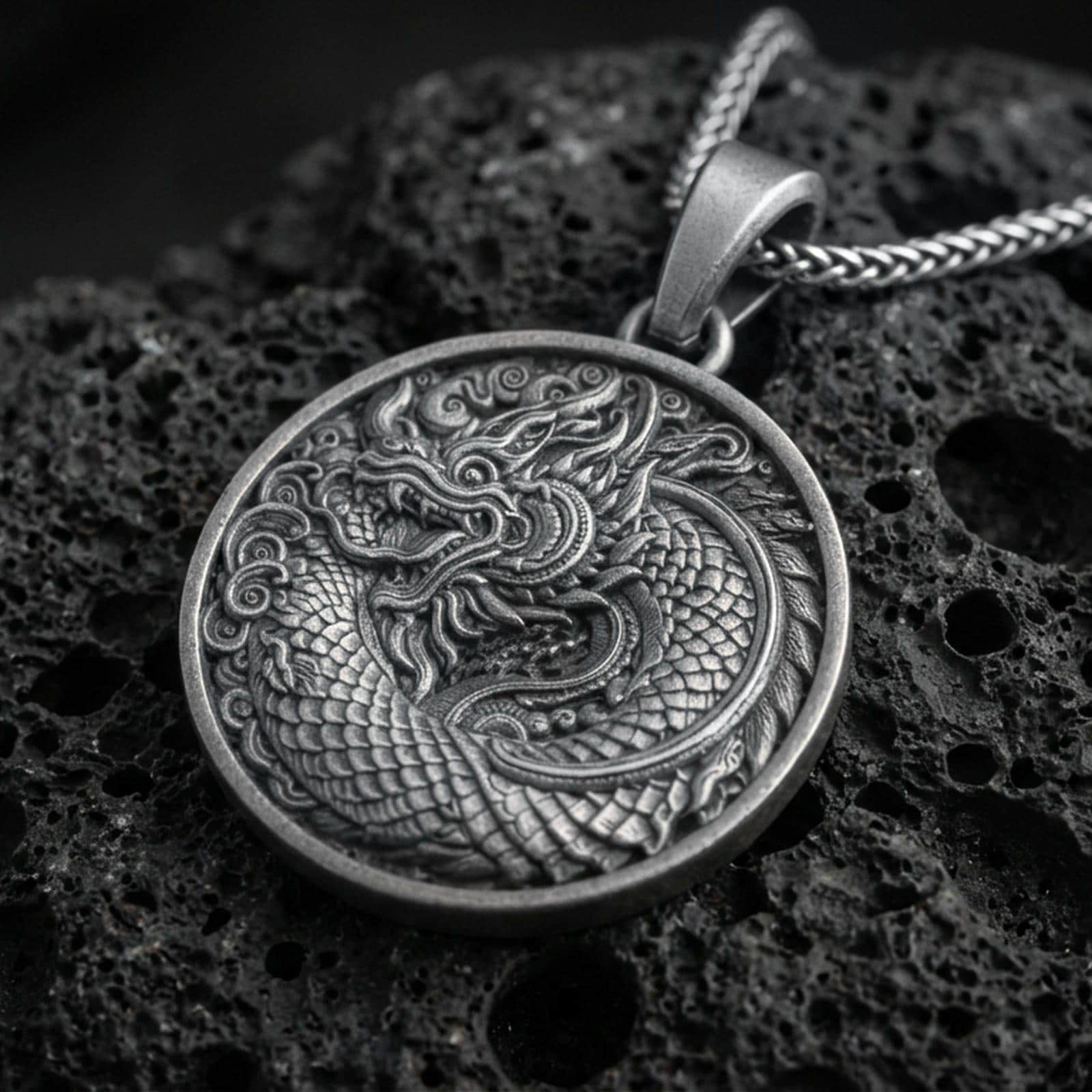 Oxidized oriental dragon medallion pendant necklace on textured volcanic rock, centered close-up highlighting the coiled Eastern dragon, layered scales, and deep antique contrast.