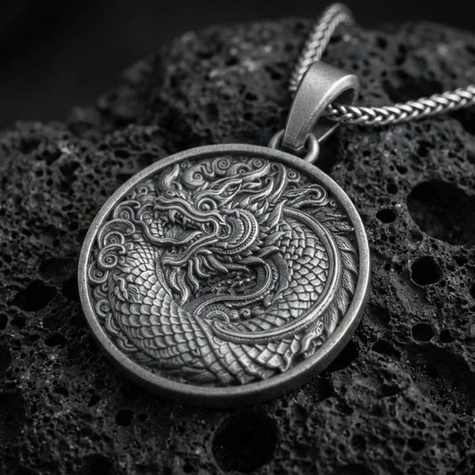 Oxidized oriental dragon medallion pendant necklace on textured volcanic rock, centered close-up highlighting the coiled Eastern dragon, layered scales, and deep antique contrast.
