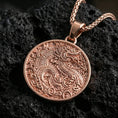 Load image into Gallery viewer, Rose gold plated dragon medallion pendant necklace on textured volcanic rock, centered studio-style close-up showcasing soft rosy glow and intricate dragon-and-cloud engraving detail.
