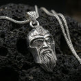 Load image into Gallery viewer, Polished silver Odin pendant necklace on textured volcanic rock, crisp macro product photo emphasizing sharp facial relief, clean edges, and detailed helmet knotwork.
