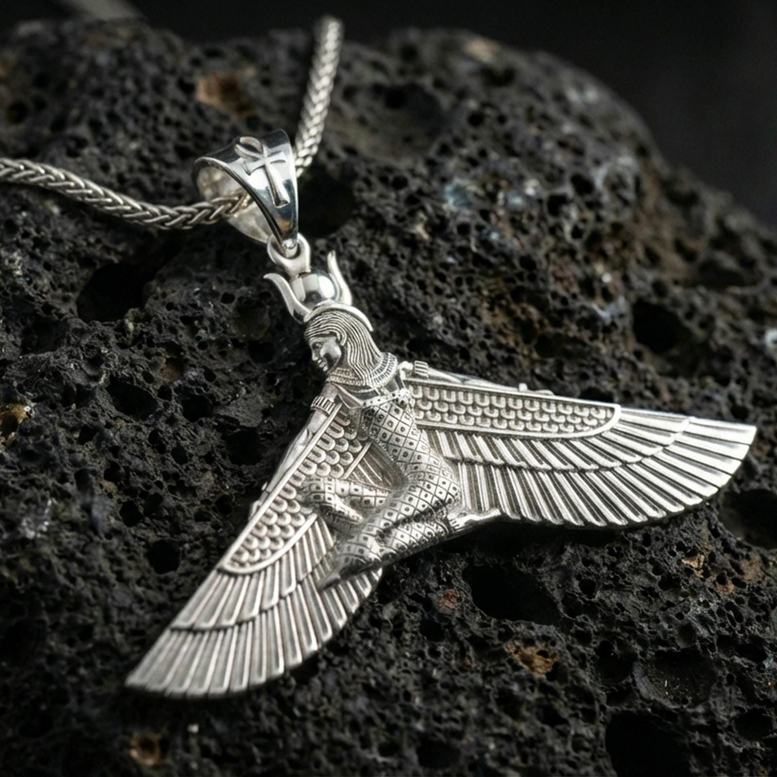 Polished silver winged goddess ankh pendant necklace on textured volcanic rock, crisp macro product photo emphasizing clean edges, sharp feather lines, and bright reflective highlights.